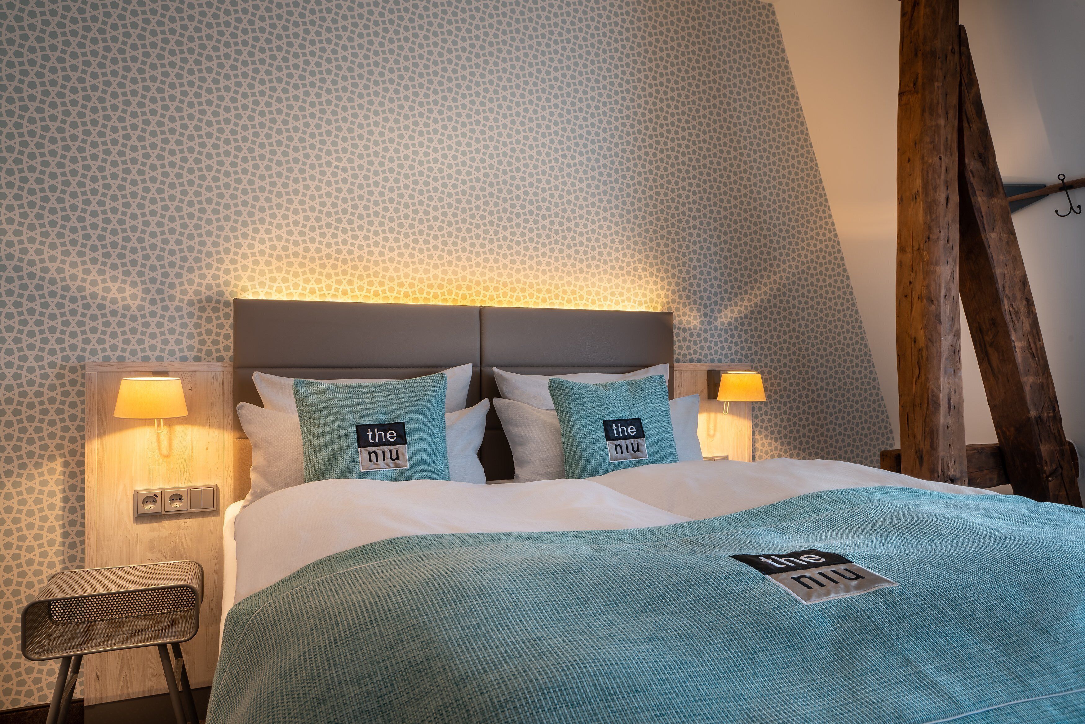 A neatly made bed with a teal bedspread and pillows labeled "the niu".
