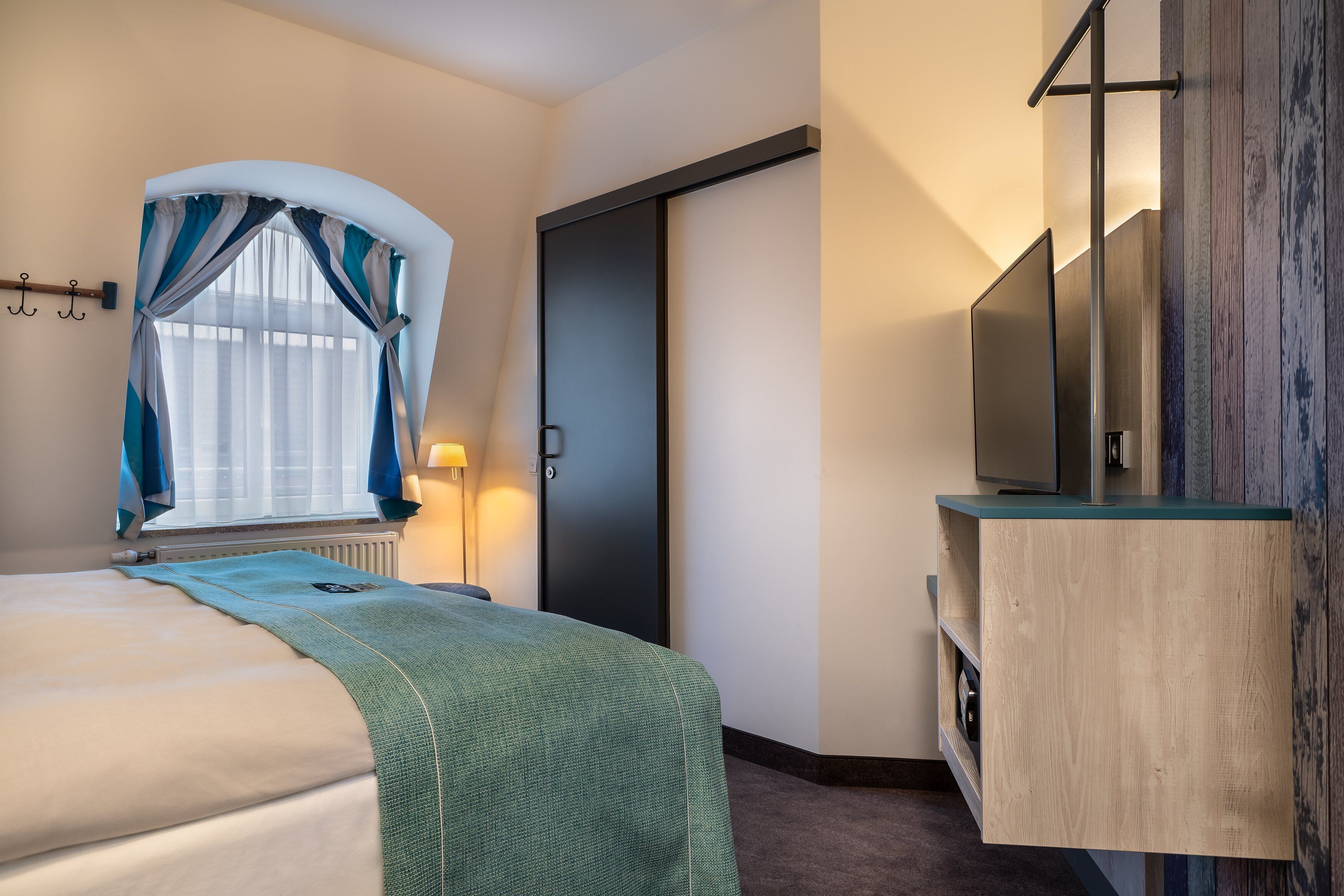 A hotel room with a bed, a TV, a wooden cabinet, and a door.