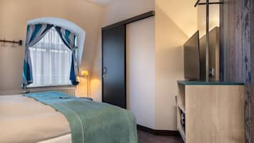 A hotel room with a bed, a TV, a wooden cabinet, and a door.