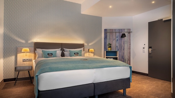 A modern bedroom with a large bed, two bedside tables with lamps, a small side table, and a wooden panel wall.