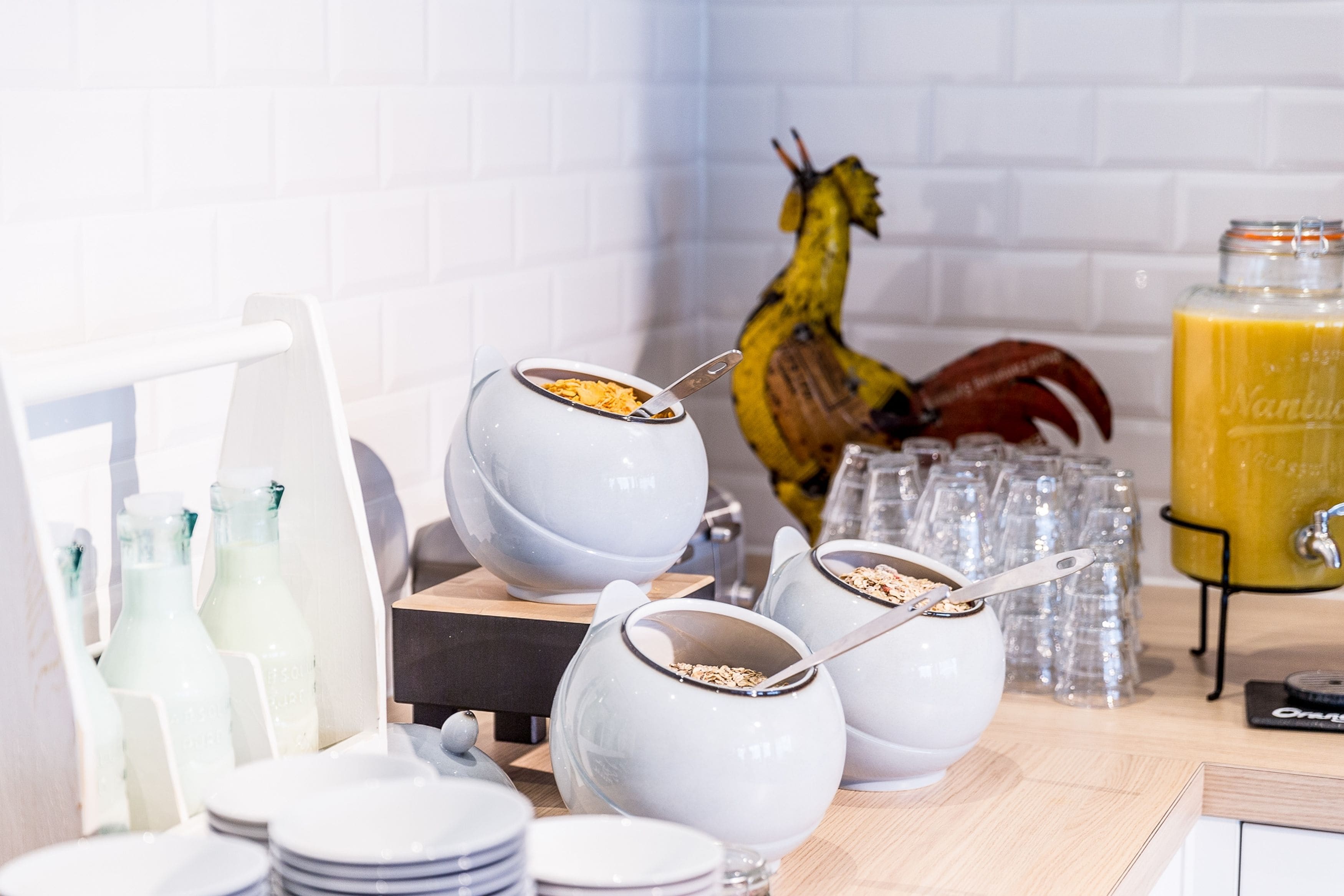 A breakfast buffet with bowls of cereal, milk bottles, and a fruit juice dispenser.