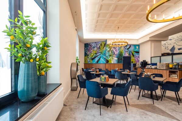 A modern dining area with blue chairs, a central table, and a large abstract painting on the wall. - Holiday Inn - the niu, Rig Lübeck by IHG (Lübeck)