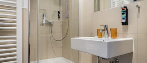Un baño moderno con cabina de ducha de vidrio, un lavabo blanco y un perchero para toallas.