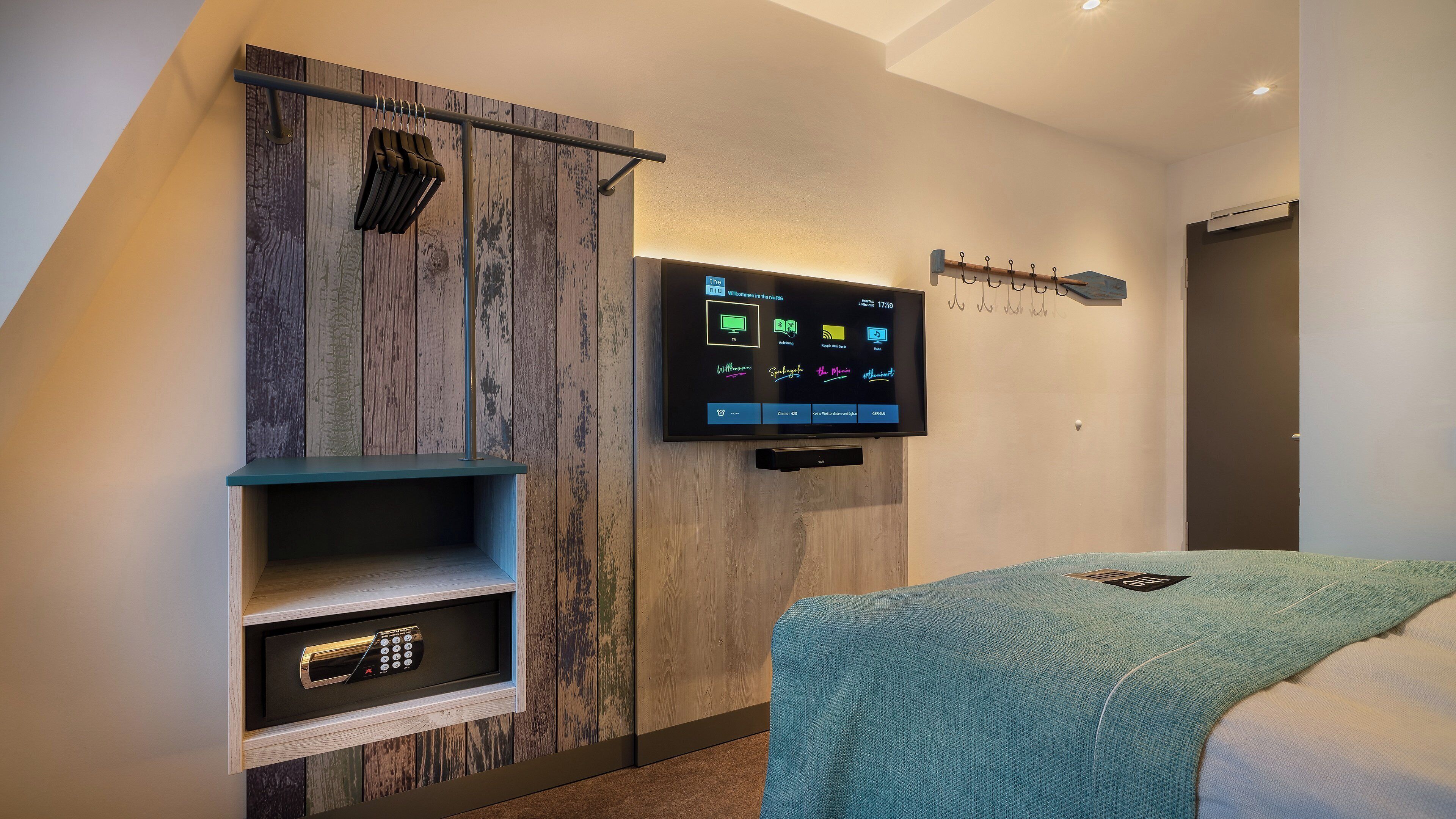 A modern hotel room with a built-in TV, a coat rack, and a wardrobe with a wooden finish.