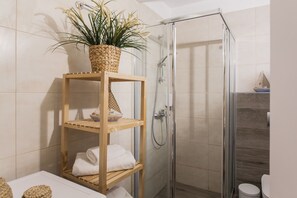 A bathroom with a glass shower enclosure, a wooden shelf with towels and a plant, and a tiled wall. - Kolonaki 2 Bedroom Apartment by Livin Urbban (Athens)