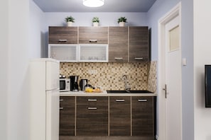 Eine kleine Küche mit dunklen Holzschränken, einem weißen Kühlschrank, einer Kaffeemaschine und einem Spülbecken.