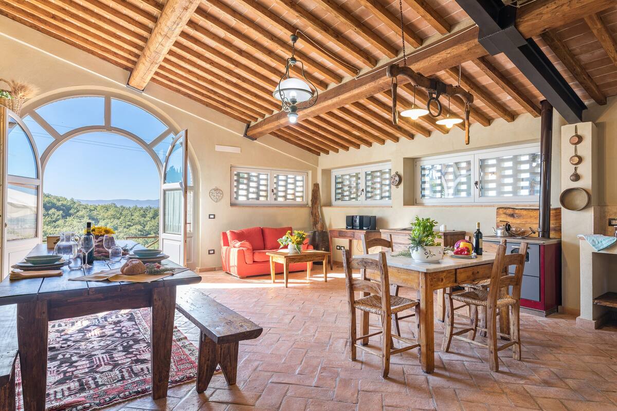 A spacious dining area with a wooden table and chairs, a red sofa, and a view of the outdoors.