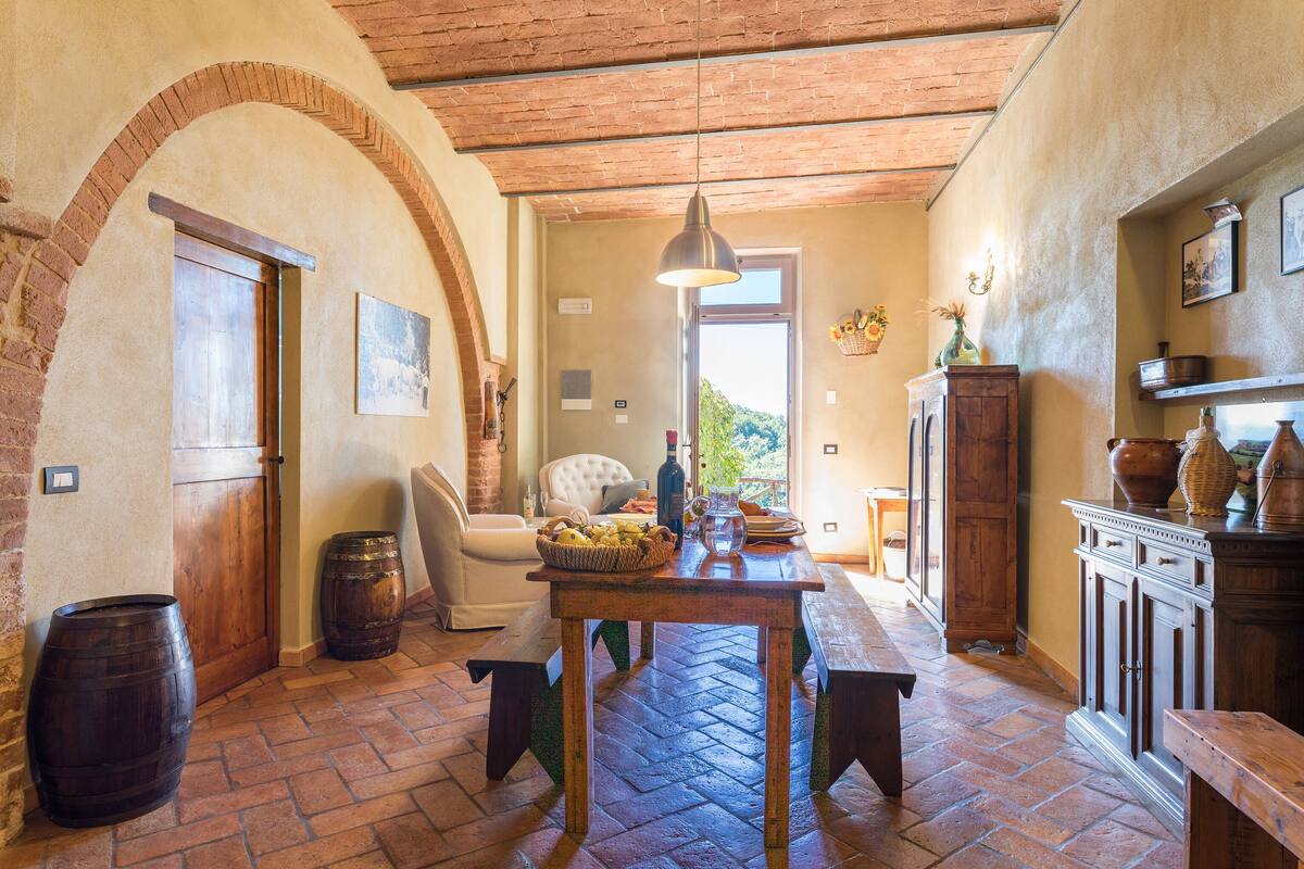 A rustic interior with a wooden table, benches, and a brick floor.