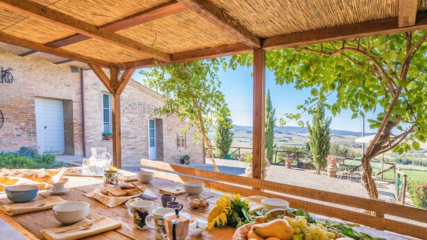 Una mesa de madera preparada para el desayuno, con vista a un edificio de ladrillo y al campo.