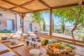 A wooden table set for breakfast with a view of a brick building and countryside. - Podere Albereto (Buonconvento)
