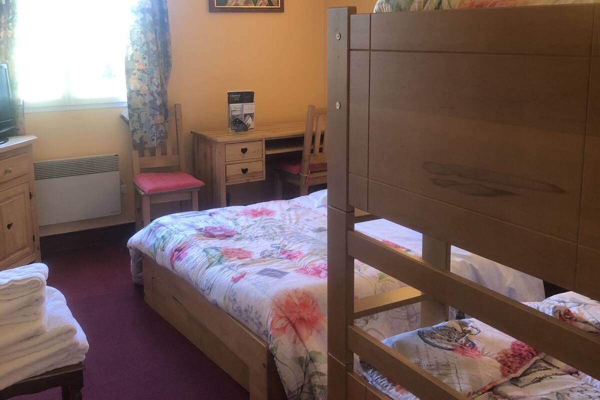 A bedroom with a bunk bed, a desk, a chair, a radiator, and a window with curtains.