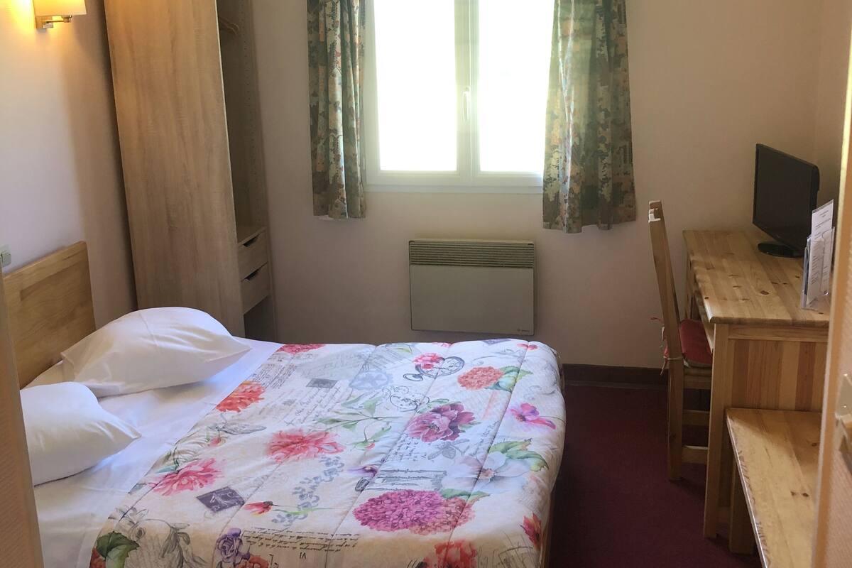 A hotel room with a bed, a desk, a chair, a television, and a window with curtains.