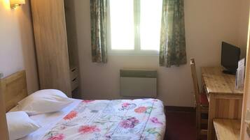 A hotel room with a bed, a desk, a chair, a television, and a window with curtains.