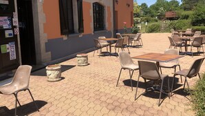 Een terras buiten met honingraatmozaïek, zitplaatsen met stoelen en tafels, en een gebouw met een bord waarop een restaurant wordt aangegeven.
