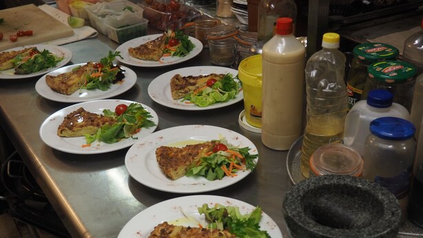 Una encimera de cocina con platos de comida, un mortero y una manoja de botellas de condimentos.