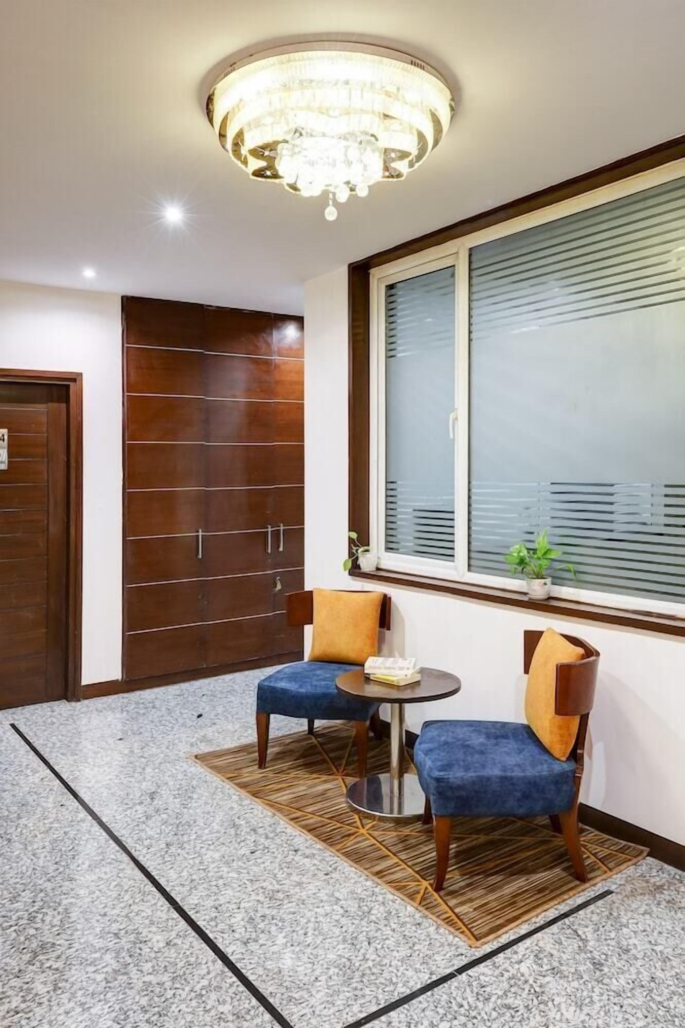 A room with a chandelier, a large window with blinds, a door, and two chairs with a small table.