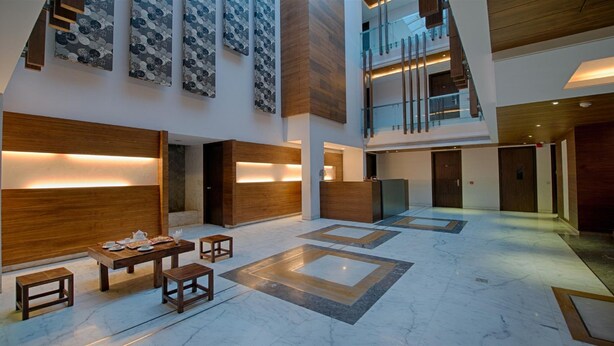 A spacious lobby with a high ceiling, a reception desk, and a staircase leading to an upper level. - Stately Suites Golf Course Road (Gurugram)