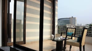 A balcony with a table and chairs, a glass door, and a view of buildings. - Stately Suites Golf Course Road (Gurugram)
