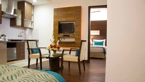 A hotel room with a bed, a dining table with chairs, a TV mounted on the wall, and a kitchenette. - Stately Suites Golf Course Road (Gurugram)