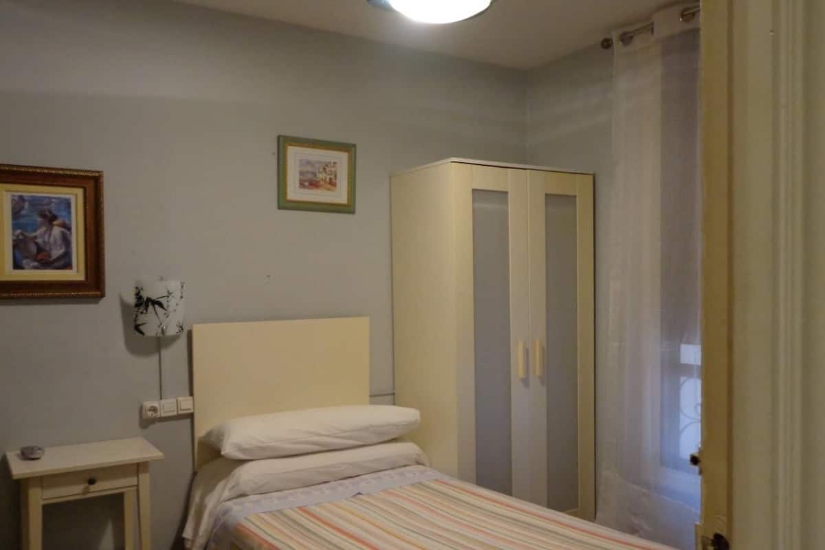Un dormitorio con una cama individual, una mesita de noche, un armario y un cuadro en la pared.
