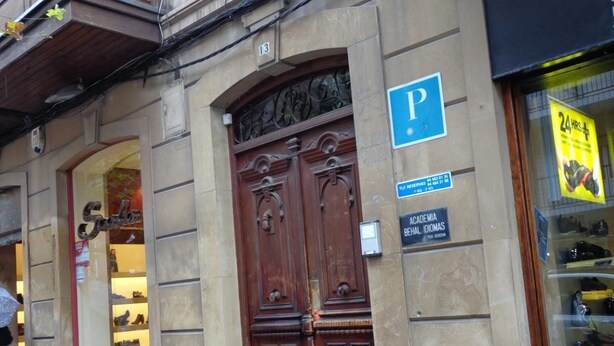 Un bâtiment doté d’une grande porte en bois, d’un panneau indiquant un parking « P » et d’une enseigne pour « Academia Chal Idiomas ».