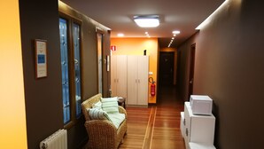 Un couloir avec un canapé en osier, des meubles blancs et un extincteur.