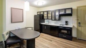 A modern kitchen with dark cabinetry, a stainless steel refrigerator, a built-in oven, and a dining area with a table and chairs. - Candlewood Suites Rochester Mayo Clinic Area by IHG (Rochester)