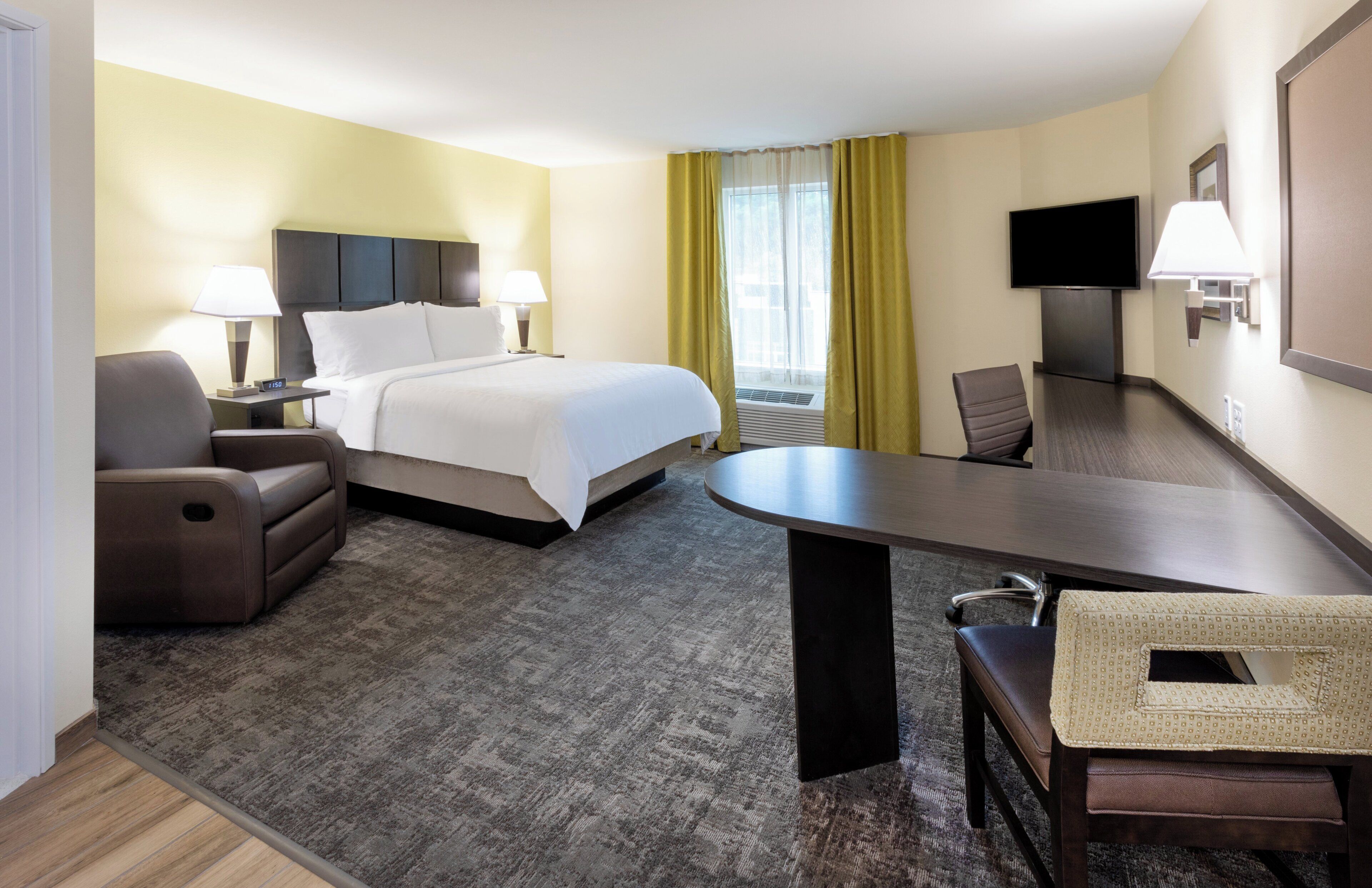 A hotel room with a bed, a desk, a chair, a TV, and a window with curtains.