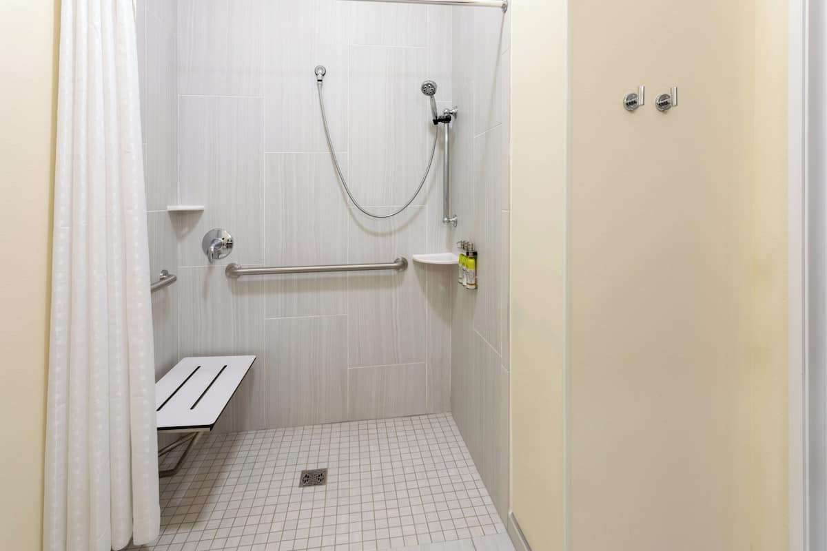 Une douche équipée d’une barre d’appui, un petit lavabo et des toilettes.
