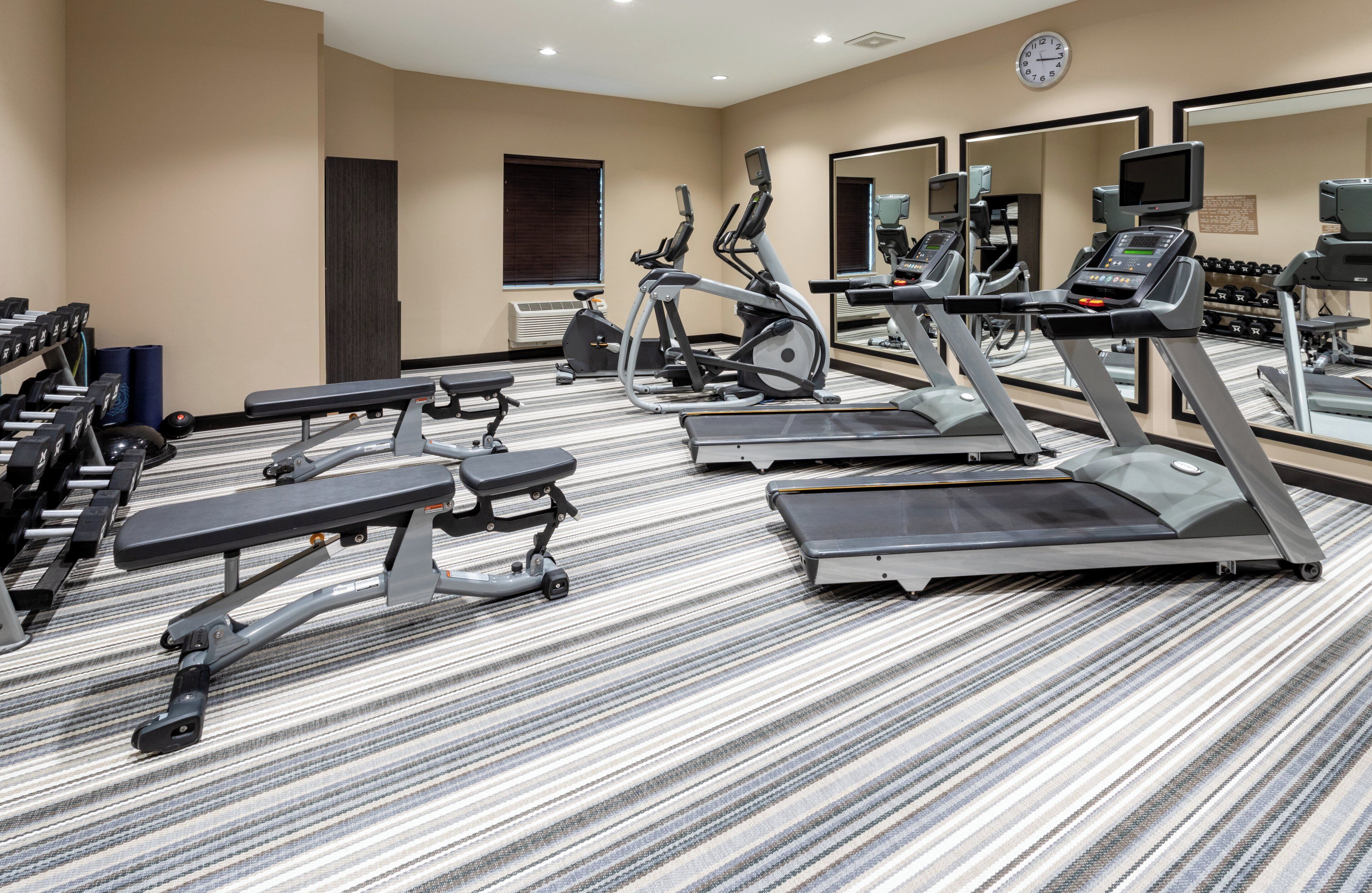 Un gimnasio de hotel con cintas de correr, elípticas y pesas sueltas.
