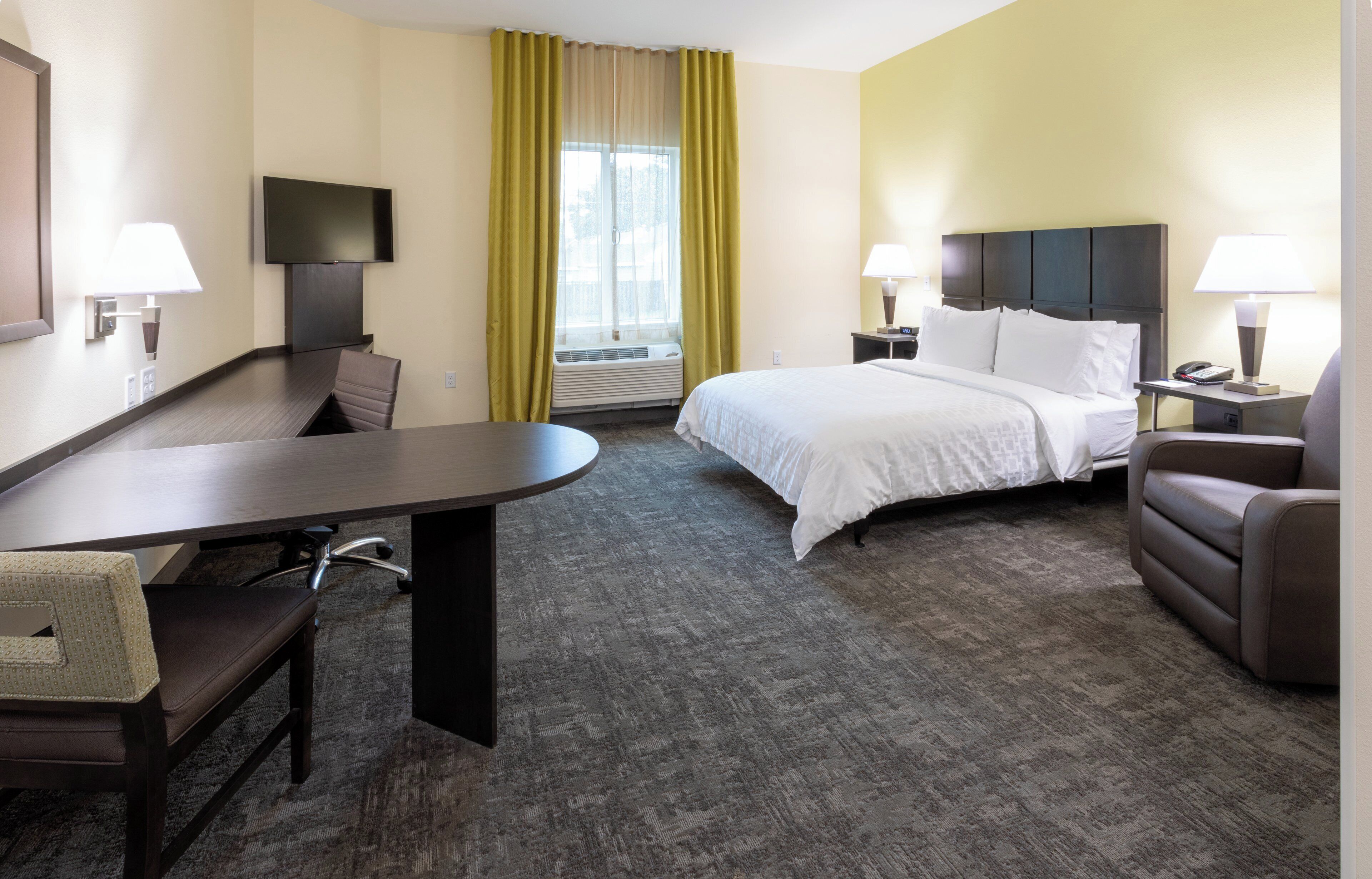 A hotel room with a bed, a desk, a chair, a TV, a window with curtains, and a nightstand with a lamp.