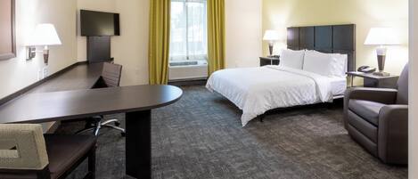 A hotel room with a bed, a desk, a chair, a TV, a window with curtains, and a nightstand with a lamp.