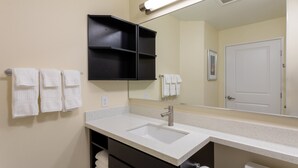 A bathroom with a double sink, a mirror, and a towel rack with multiple towels. - Candlewood Suites Rochester Mayo Clinic Area by IHG (Rochester)