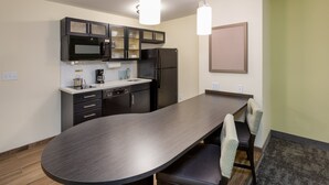 A modern kitchen with a dark countertop, black cabinets, a microwave, and a refrigerator. There are two pendant lights above the counter. - Candlewood Suites Rochester Mayo Clinic Area by IHG (Rochester)
