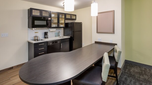 A modern kitchen with a dark countertop, black cabinets, a microwave, and a refrigerator. There are two pendant lights above the counter. - Candlewood Suites Rochester Mayo Clinic Area by IHG (Rochester)