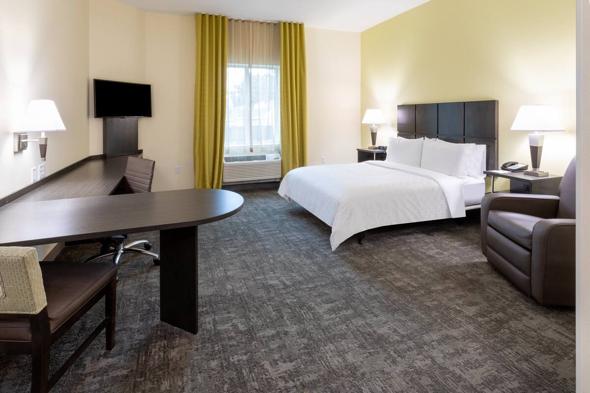 Une chambre d’hôtel avec un lit, un bureau, une chaise, une télévision et une fenêtre avec des rideaux.