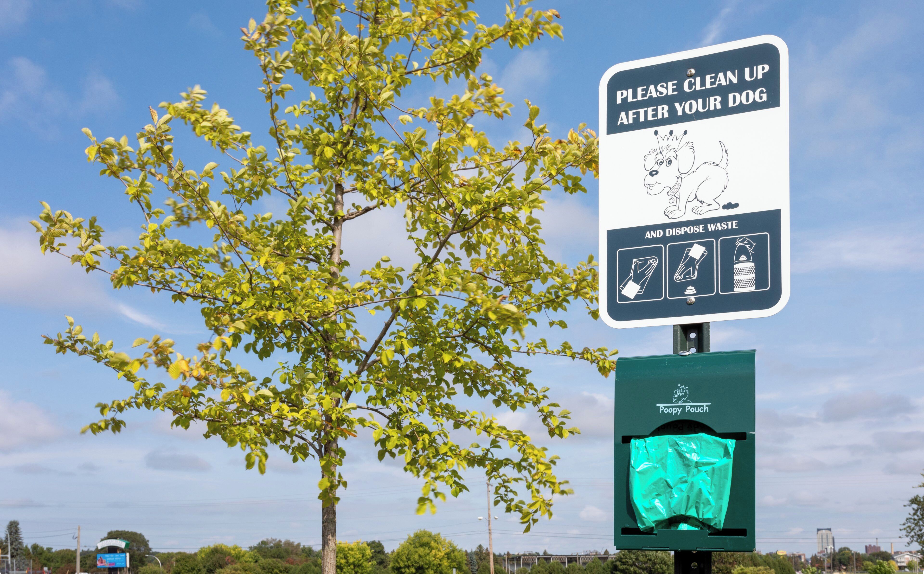 A sign instructing to clean up after dogs and dispose of waste, with a Poopy Pouch attached.