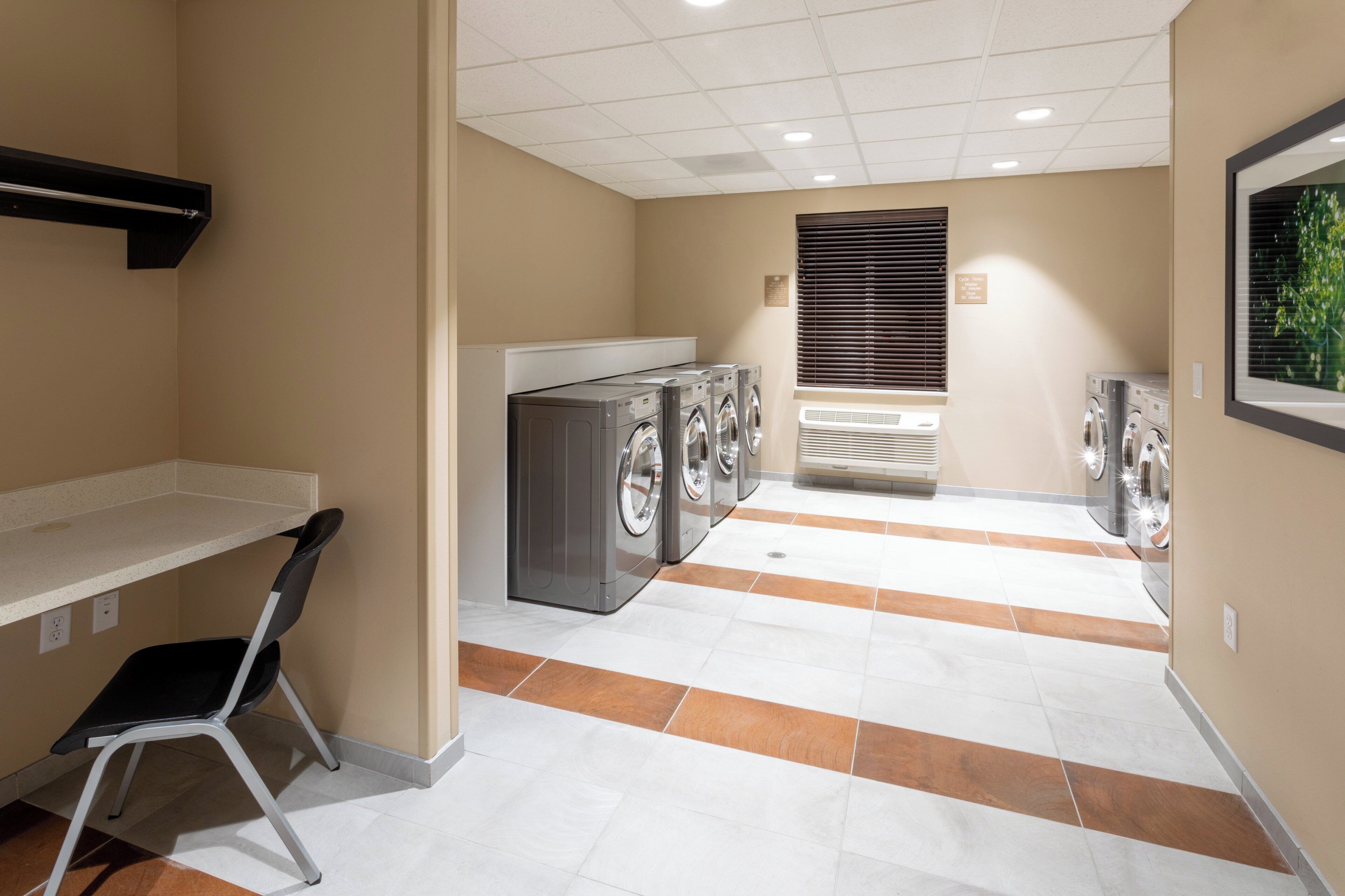 A laundry room with multiple washing machines and dryers, a chair, and a vented window.