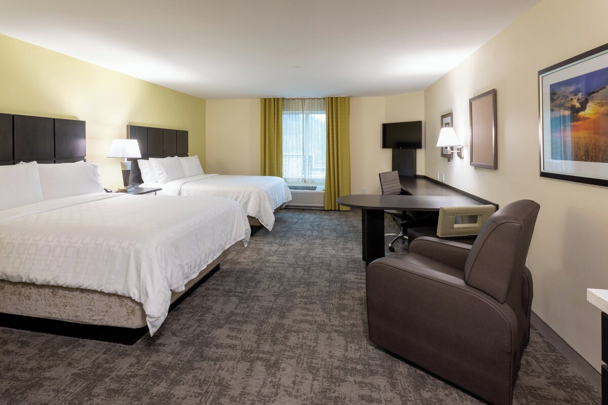 A hotel room with two beds, a desk, a chair, a TV, and a window with curtains.