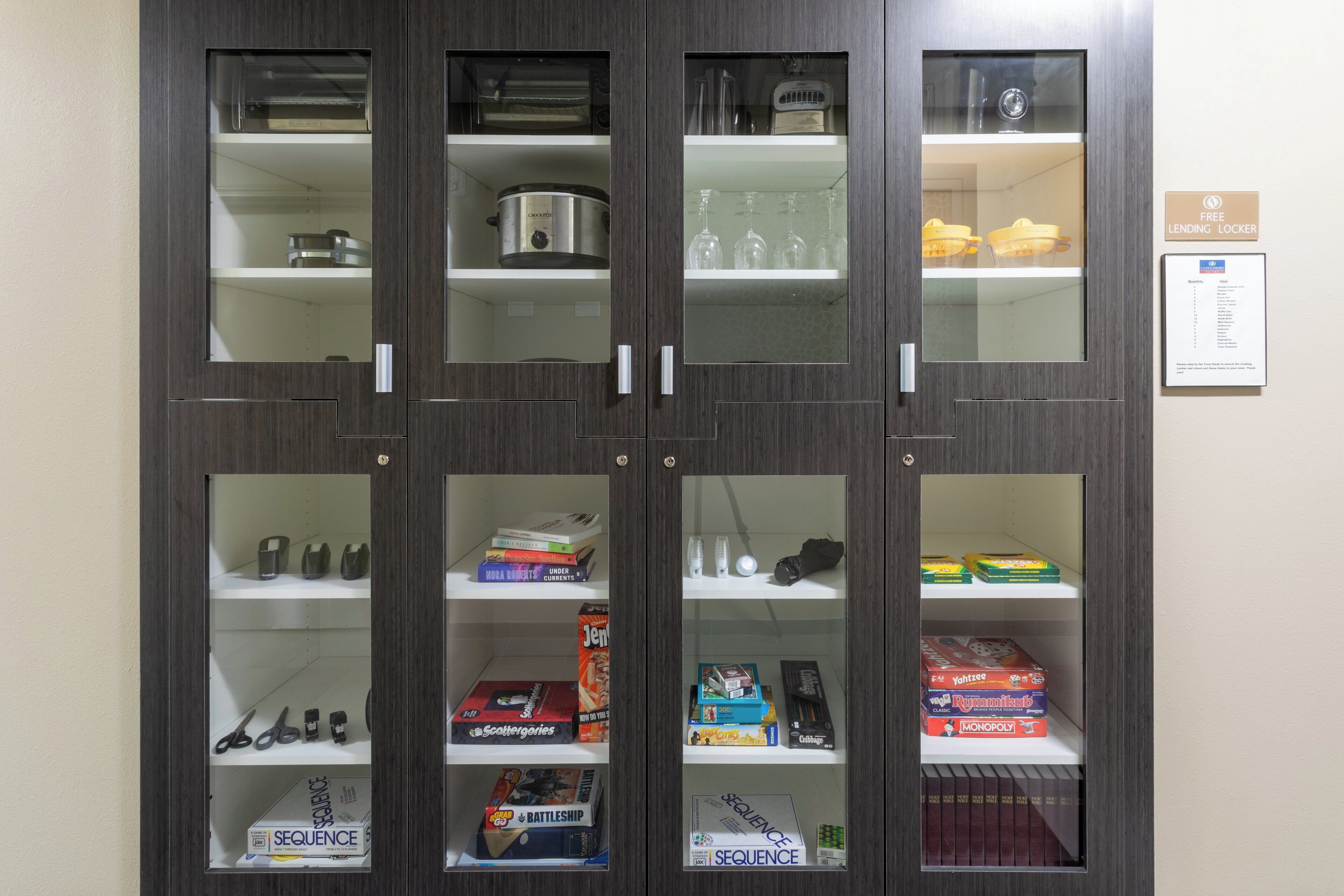 A storage cabinet with multiple shelves containing kitchen appliances, glassware, and board games.