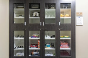 A storage cabinet with multiple shelves containing kitchen appliances, glassware, and board games. - Candlewood Suites Rochester Mayo Clinic Area by IHG (Rochester)