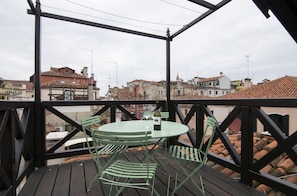 Un balcon avec une table ronde et deux chaises, donnant sur un paysage urbain avec des toits recouverts de tuiles en terre cuite.