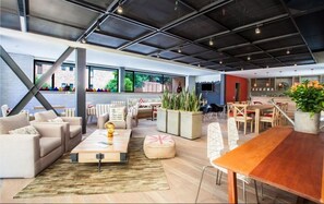A spacious living area with a large wooden table, sofas, and a coffee table. There are potted plants and a TV mounted on the wall. - Mika Suites (Bogotá)