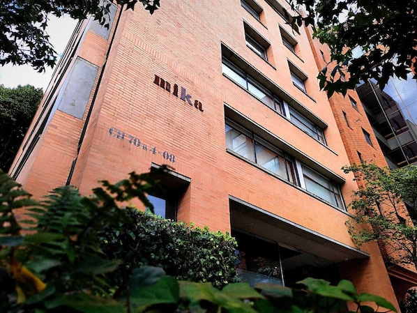 A multi-story building with a brick facade, large windows, and a visible entrance. - Mika Suites (Bogotá)