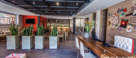 A modern interior with a wooden reception desk, seating area with potted plants, and a wall adorned with travel-themed stickers.