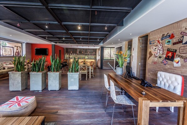 A modern interior with a wooden reception desk, seating area with potted plants, and a wall adorned with travel-themed stickers.