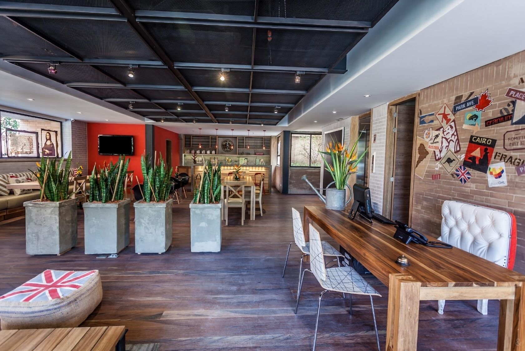 Un interior moderno con un mostrador de recepción de madera, zona de estar con plantas en macetas y una pared decorada con pegatinas de temática de viajes.