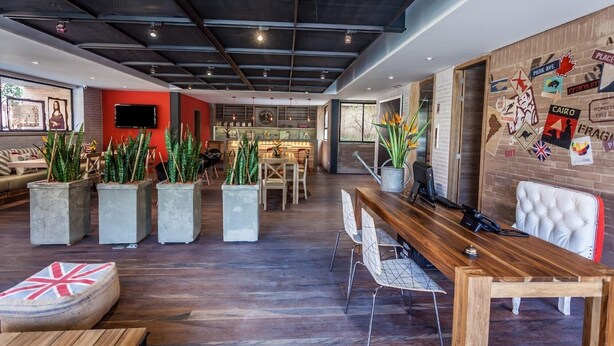 A modern interior with a wooden reception desk, seating area with potted plants, and a wall adorned with travel-themed stickers. - Mika Suites (Bogotá)