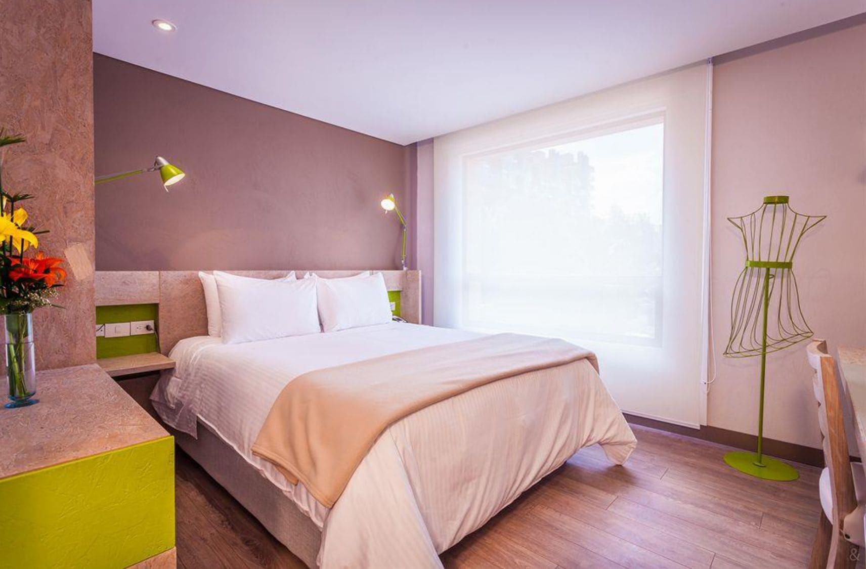 Une chambre d’hôtel moderne avec un grand lit, des lampes de chevet, une fenêtre donnant sur un beau paysage et un lampadaire vert.