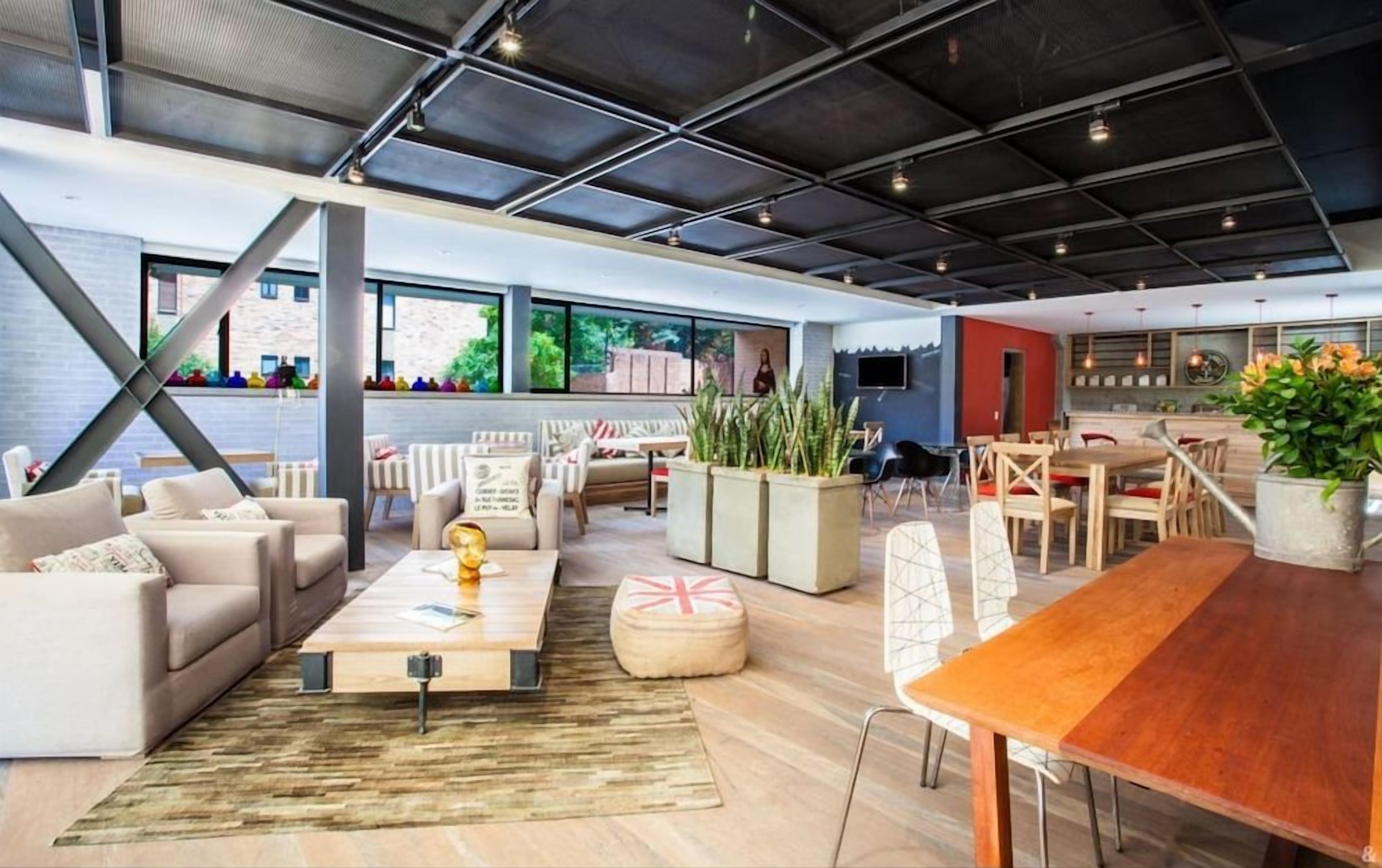 A spacious living area with a large wooden table, sofas, and a coffee table. There are potted plants and a TV mounted on the wall.